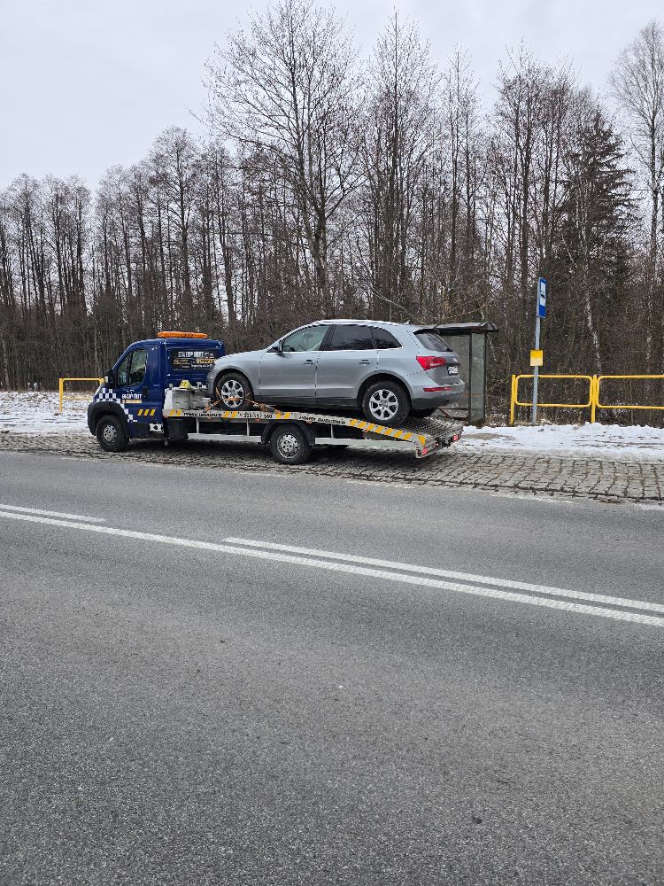Holowanie SUV-a na lawecie zimą, przy drodze przez las